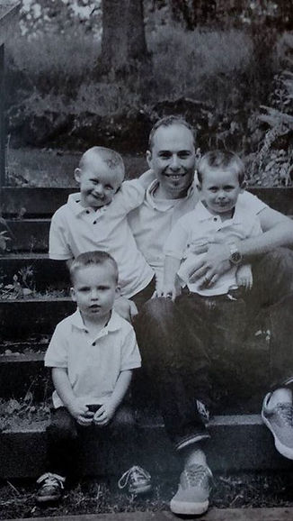 Father sitting outdoors with three young boys